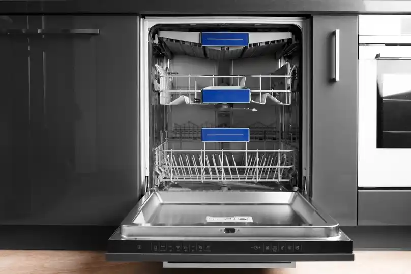 The image shows an open, built-in dishwasher integrated into a modern kitchen setup. The dishwasher is completely empty and clean, revealing its three rack levels.